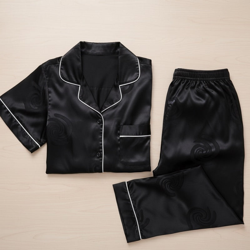 Black satin pajama set with white piping on a beige background