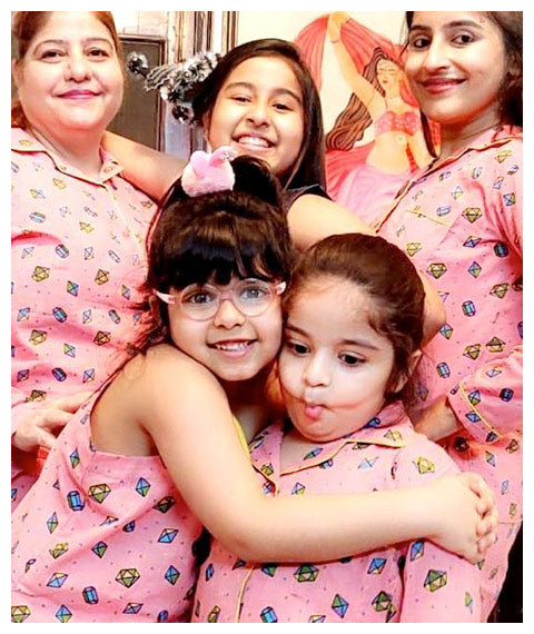 Two young girls in pink pajamas with a woman in a similar pajama, all smiling.