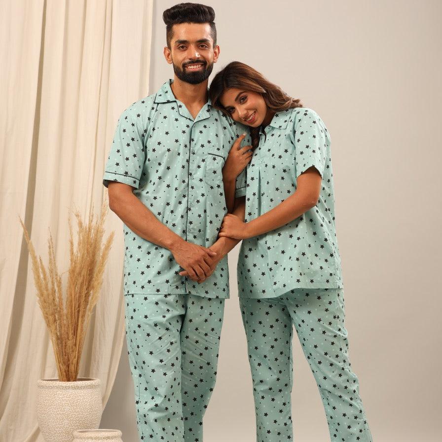 Man and woman wearing matching light blue pajamas with a pattern, standing against a neutral background.