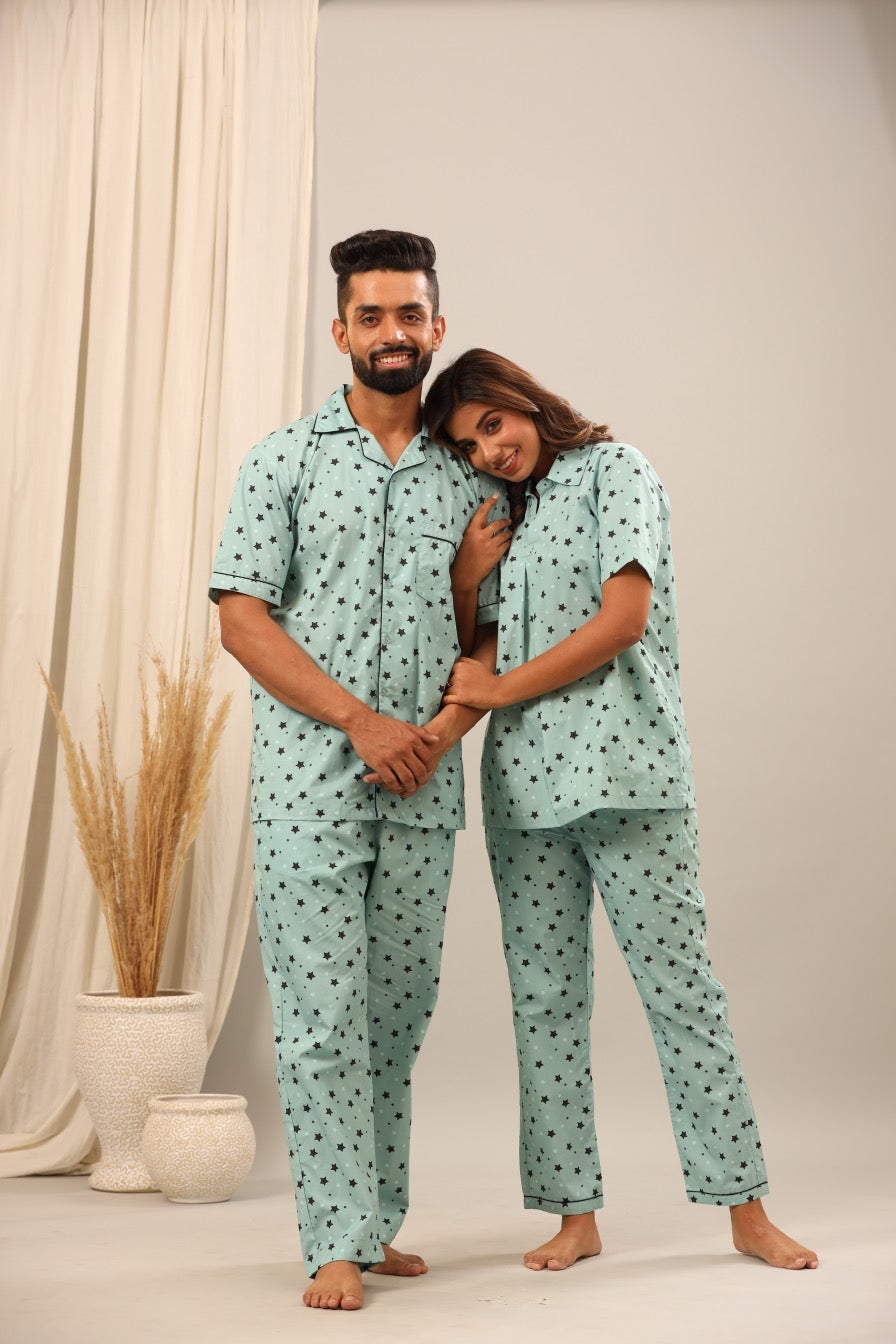 Man and woman wearing matching light blue pajamas with a pattern, standing against a neutral background.