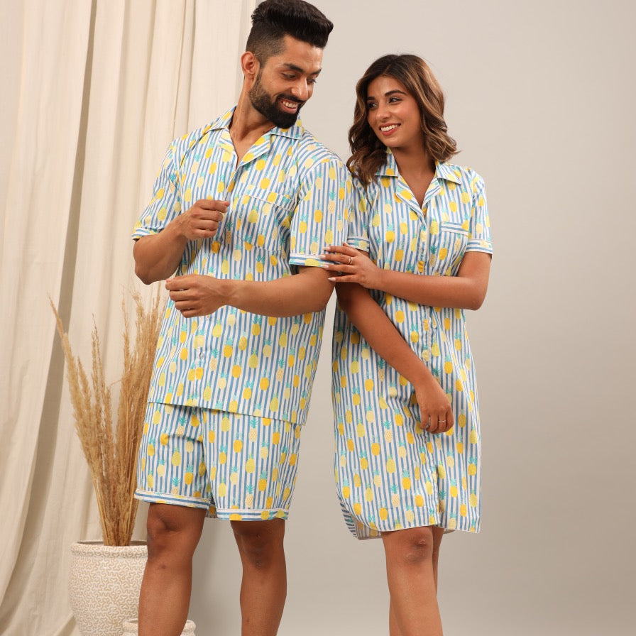 Husband and wife wearing matching blue and yellow patterned pajama sets standing against a neutral background.