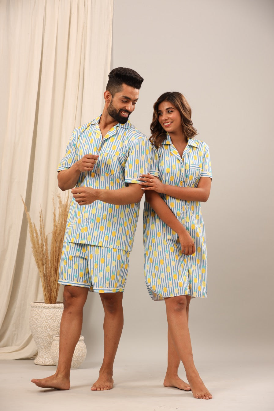 Husband and wife wearing matching blue and yellow patterned pajama sets standing against a neutral background.
