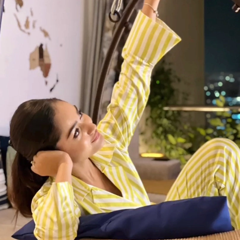 Woman in yellow and white striped super luxe satin night suit relaxing on a chair.