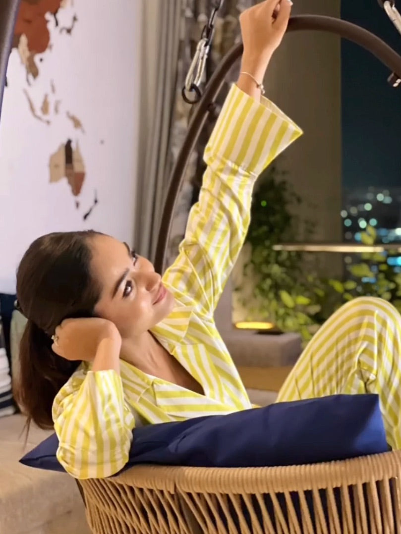 Woman in yellow and white striped super luxe satin night suit relaxing on a chair.