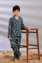 Boy wearing 100% cotton Christmas print pajama set standing next to a wooden stool