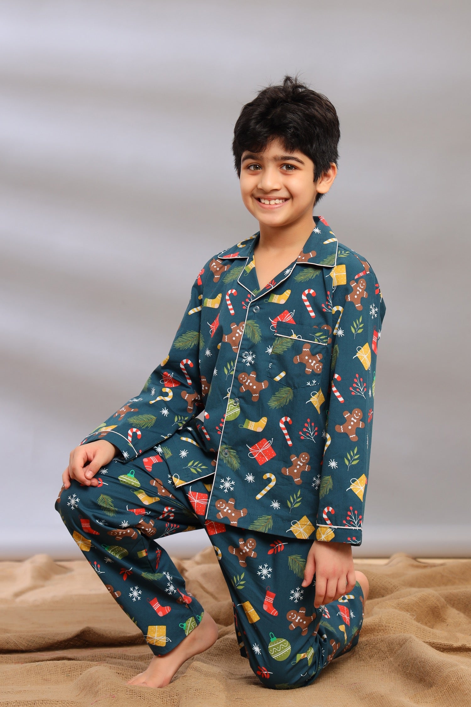 Boy wearing festive Christmas pajamas with a pattern of Christmas elements on a neutral background