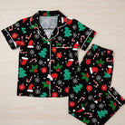 Christmas-themed pajama set with black background featuring red, green, and white patterns on a light wooden surface.