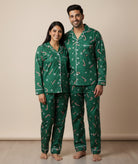 Man and woman wearing matching green pajama sets with candy cane pattern on a beige background
