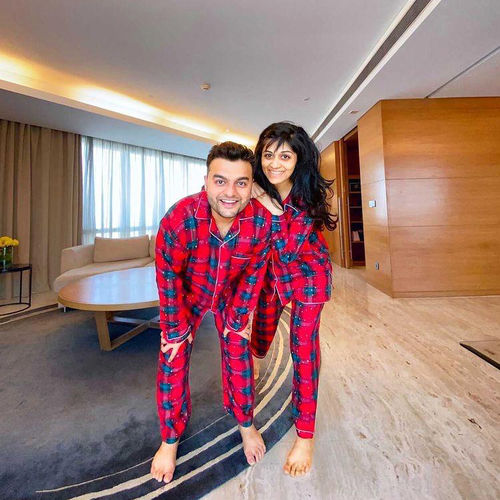 Couple in Christmas red plaid pajamas posing in a modern living room.