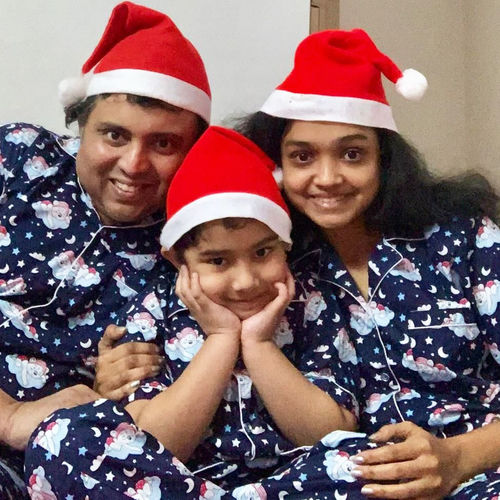 Family of three wearing matching pajamas and Santa hats indoors.