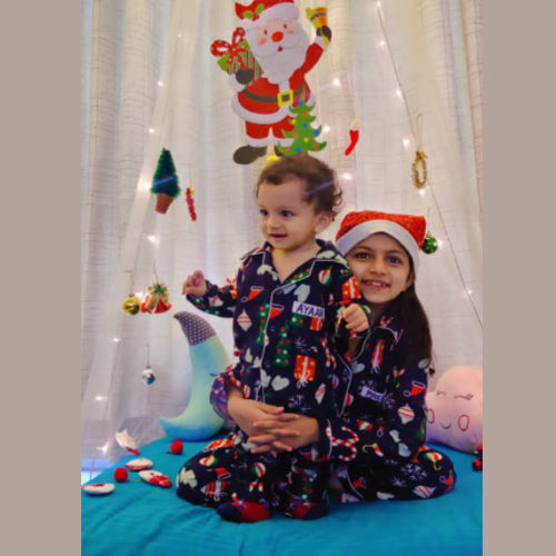 Two children in Christmas themed  pajamas with Christmas decorations in the background