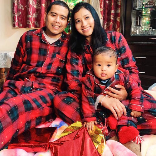 Family of three wearing Christmas themed red plaid matching night suits sitting together.