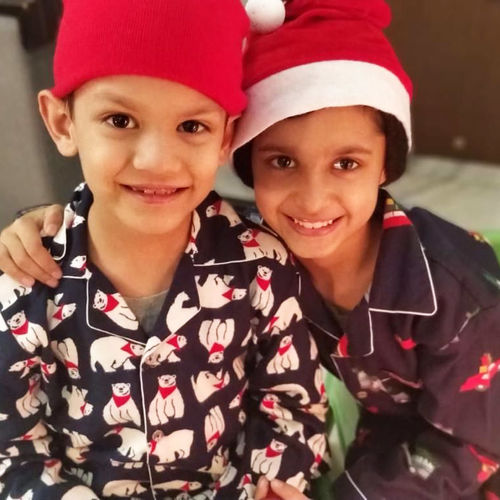 Two children wearing festive Christmas  sleepwear with red hats, smiling at the camera.