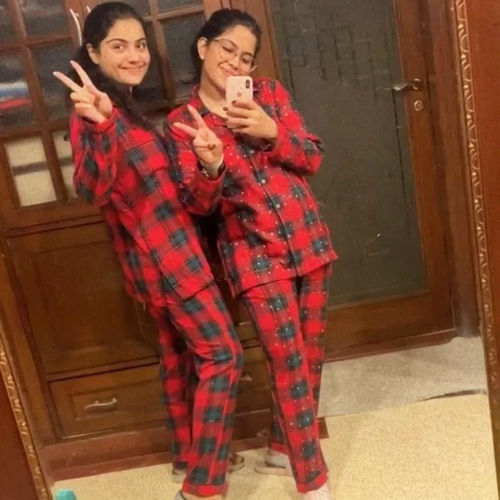 Two sisters wearing red and black checkered pajamas taking a mirror selfie.
