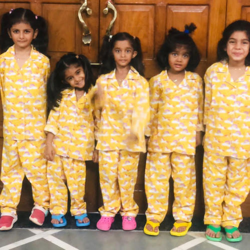 Five children wearing matching yellow pajama sets in front of a wooden door.