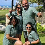 Family of four posing together outdoors with palm trees and a beach in the background