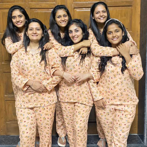 Six women in matching pajama sets posing together in front of a wooden door.