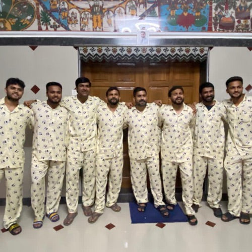 Group of men wearing matching pajamas posing for a photo in a room with decorative walls.