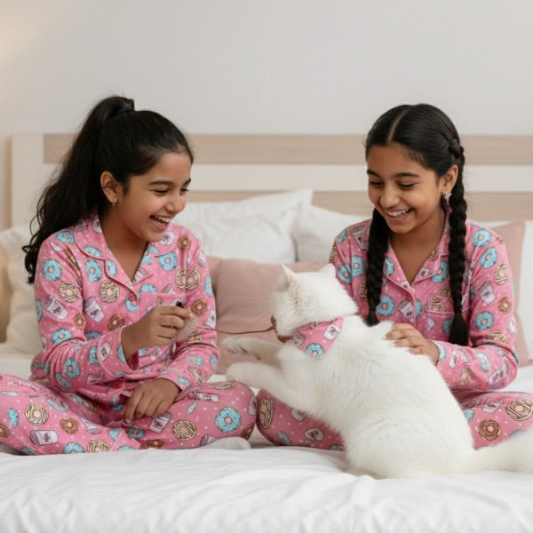 Two children in pink pajamas with a white cat on a bed.