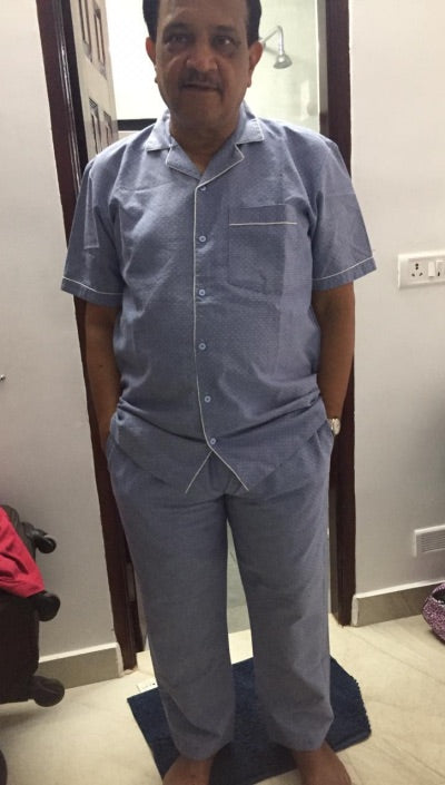 Man wearing a blue pajama set standing in a room with a neutral background.
