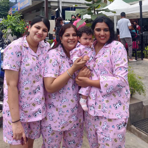 Three women in matching pink pajama sets with a baby held by one of them, outdoors.