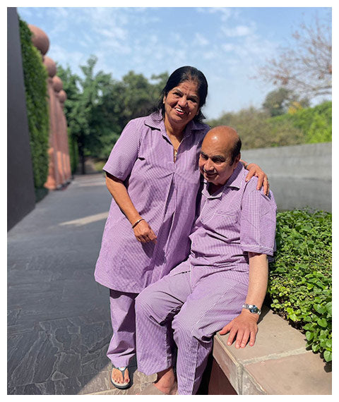Two elderly people in matching purple pajama set sitting outdoors on a sunny day.