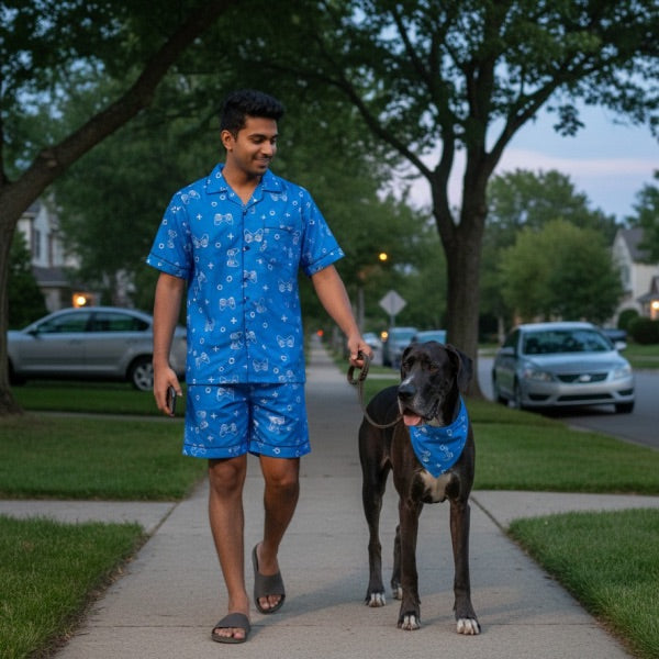 Man in blue shorts set walking a dog on a sidewalk with cars and trees in the background